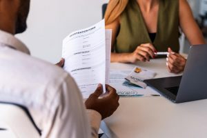 African descent gentleman reading a trust registration form while a lady is seated across him with a laptop open and pen in hands | Netsheria LLP Legal Alerts